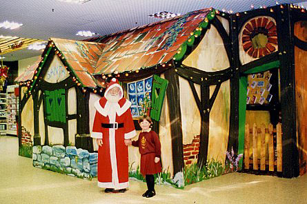 "Santa" and child customer pose before a cotttage grotto